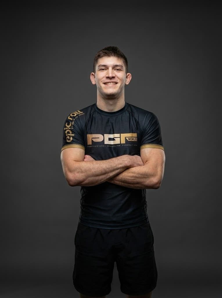 Travis Haven in a black and gold PGF rash guard, standing with his arms folded.